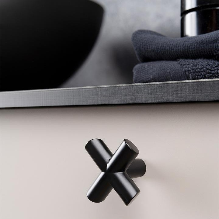 EQUIS kreuzförmiger Zamakknopf im Industrial-Design an einer modernen Möbeltür montiert.